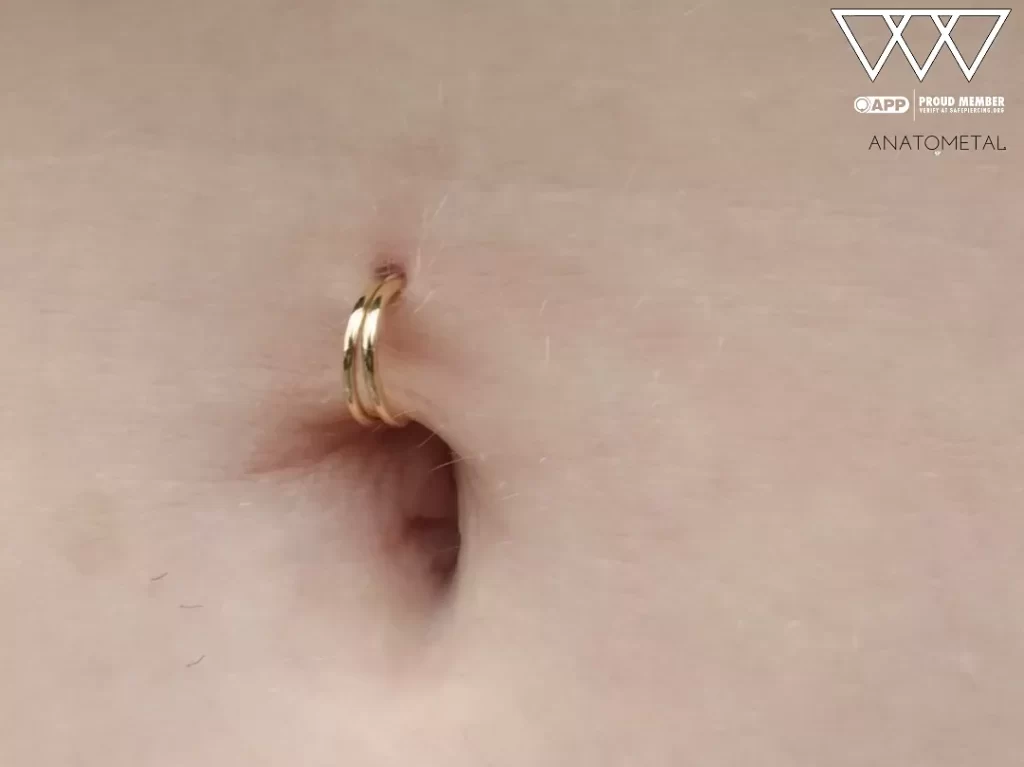 side angle photo of a navel piercing fitted with two 18k gold seam rings from Anatometal, creating a sleek, minimalist look with high-polish finishes and elegant symmetry.