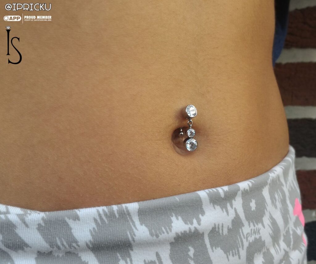 Close-up of a healed navel piercing fitted with a top-hanging titanium curved barbell featuring bezel-set clear Swarovski gemstones from Industrial Strength, showcasing the jewelry's sparkle and secure placement.