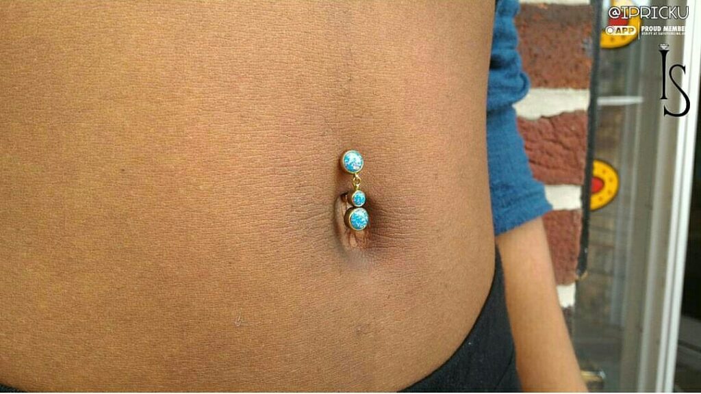 Side view of an upper navel piercing featuring a titanium bezel-set opal cabochon navel curve from Industrial Strength, showcasing the top-hanging design and anodized finish.