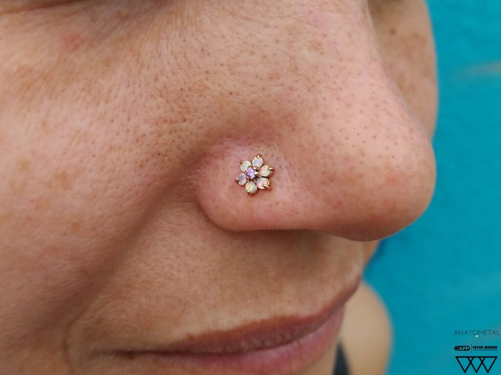 Nostril piercing featuring an 18k rose gold flower end from Anatometal, adorned with genuine opals and amethyst, showcasing intricate design and precise placement.