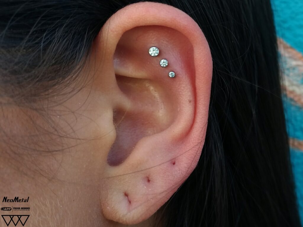Close-up of a triple flat piercing featuring three bezel-set cubic zirconia gemstones from NeoMetal, aligned vertically along the ear’s flat cartilage, showcasing precise placement and elegant sparkle.