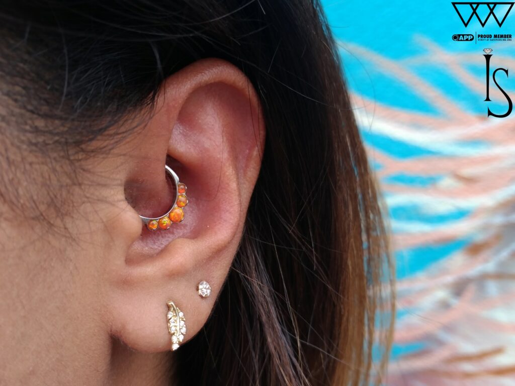 Private Body Piercing Near Edison. Expert Care, High-End Jewelry Daith piercing adorned with an Odyssey septum clicker from Industrial Strength, featuring vibrant orange opals that add a striking pop of color.