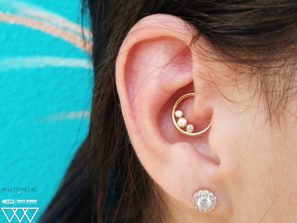 Healed daith piercing featuring an 18k gold fixed cluster seam ring from Anatometal. The polished gold finish and clustered design add a refined and elegant touch to the ear's inner cartilage fold.