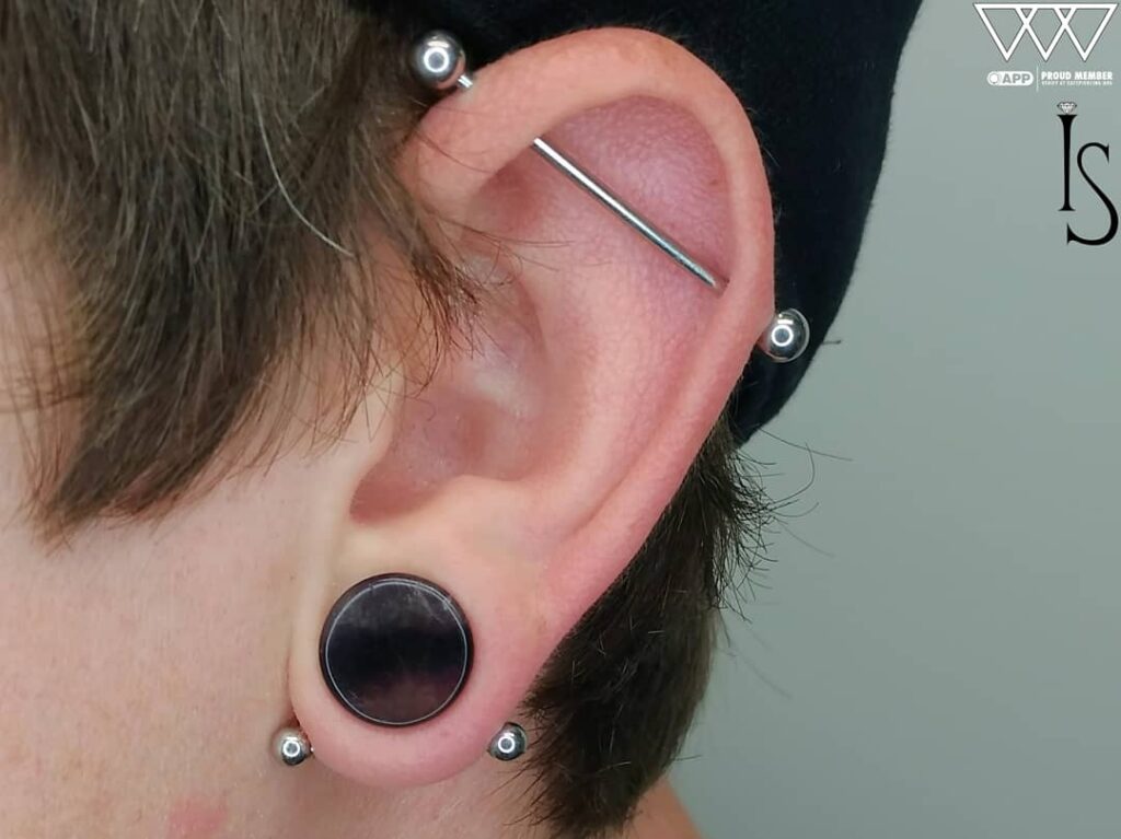 Close-up of a transverse lobe piercing on the right ear with a straight titanium barbell from Industrial Strength. The clean, horizontal alignment and high-polish finish provide a modern, minimalist accent.
