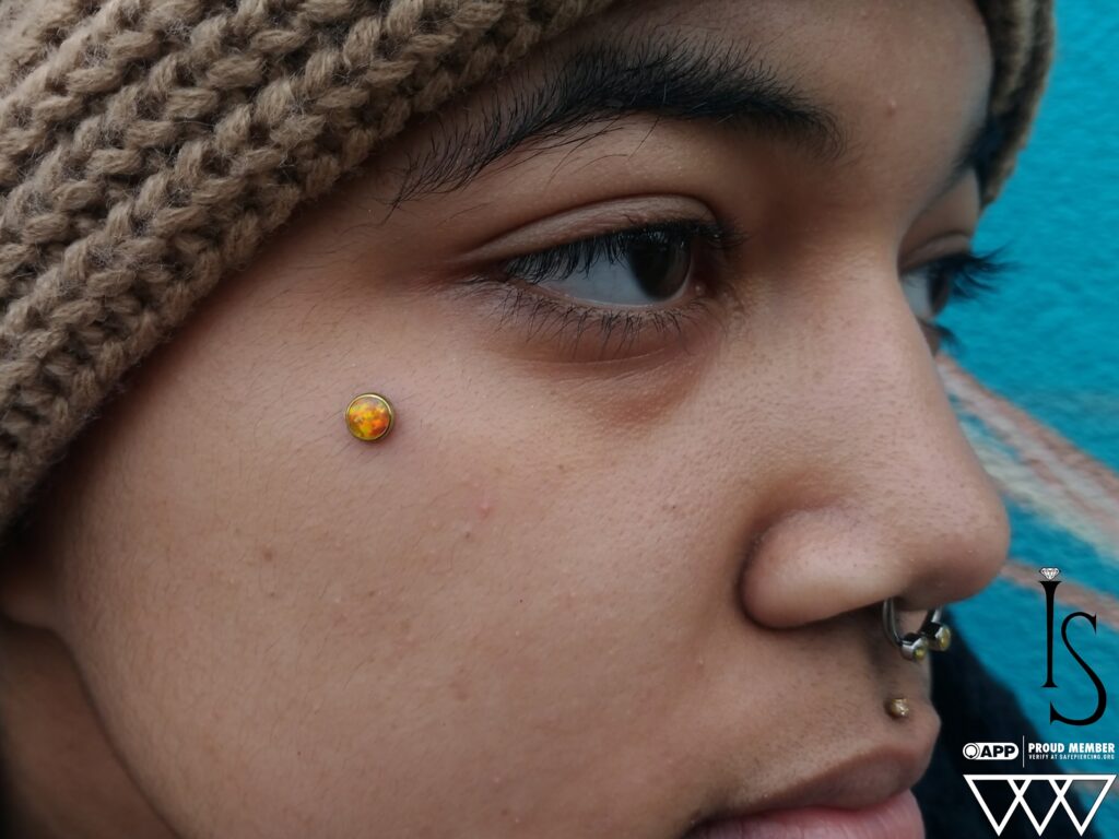 Professional Piercing Studio Near Jersey City. Private Appointments Only Close-up of a microdermal piercing featuring a bezel-set orange opal from Industrial Strength, highlighting the vibrant gemstone and precise placement.