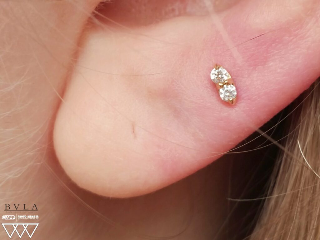 Piercing Studio Near Elizabeth, Bayonne & Union County. Private, Appointment-Only Sessions Close-up of a lobe piercing featuring a 14k gold “Marquise Illusion” threadless end from BVLA. The gem's unique cut mimics the appearance of a marquise shape, adding a touch of elegance to the earlobe.