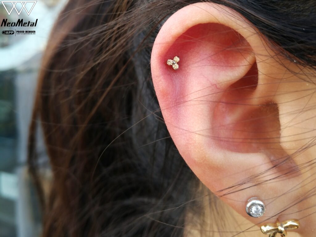Close-up of a helix piercing featuring a titanium Trinity Cluster from NeoMetal, positioned on the upper ear cartilage. The trio of polished beads adds a minimalist and elegant touch to the ear's natural curve.