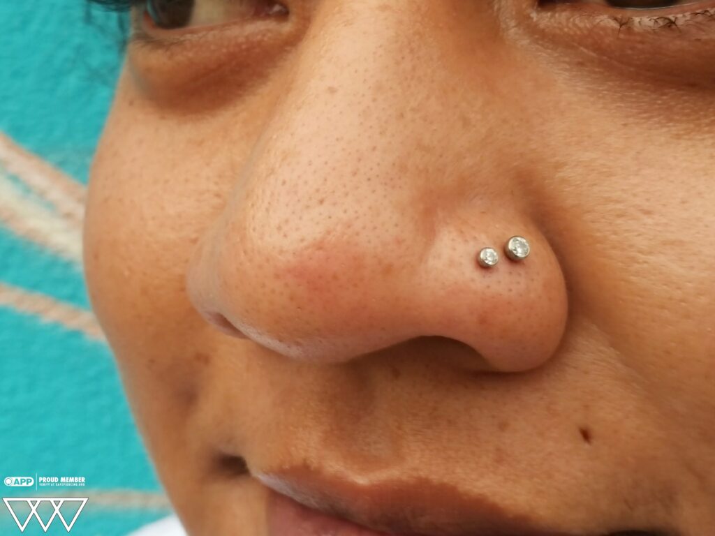 A double nostril piercing featuring titanium bezel-set gemstone ends from NeoMetal, captured during the downsizing process to ensure optimal fit and comfort.