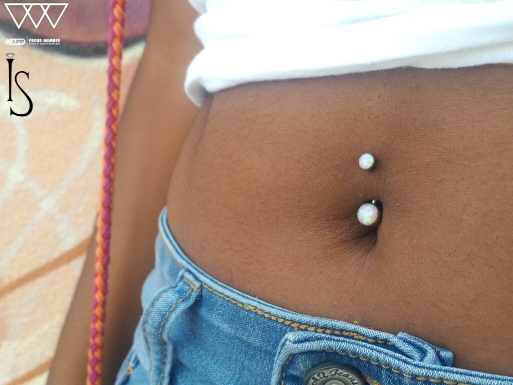 A navel piercing featuring a titanium curved barbell from Industrial Strength, set with vibrant bubblegum opals that add a playful pop of color to the belly button area.
