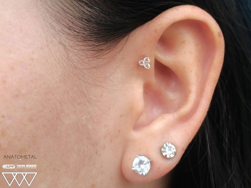 Forward Helix Piercing in Staten Island, NYC | Professional Piercing Close-up of a forward helix piercing featuring an 18k gold 'Trio' end from Anatometal, showcasing three clustered Swarovski gems in a minimalist, elegant design.