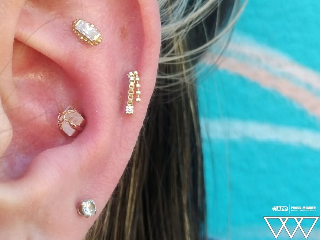 Close-up of a curated ear featuring flat, conch, and helix piercings adorned with 14k yellow gold jewelry from Pupil Hall, including a BVLA “Beaded Baguette” in the flat piercing, showcasing a cohesive and elegant ear design.