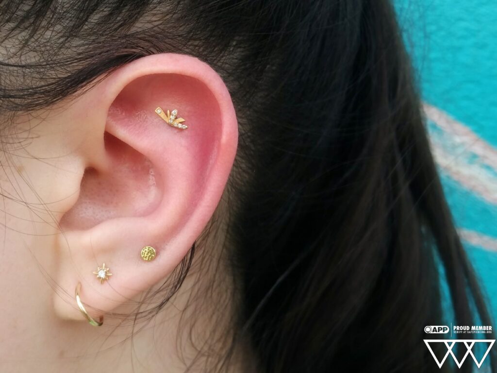 Close-up of a flat piercing adorned with a 14k gold 'Flutter' end from Pupil Hall, featuring genuine diamonds, highlighting the elegant design and precise placement on the ear's cartilage.