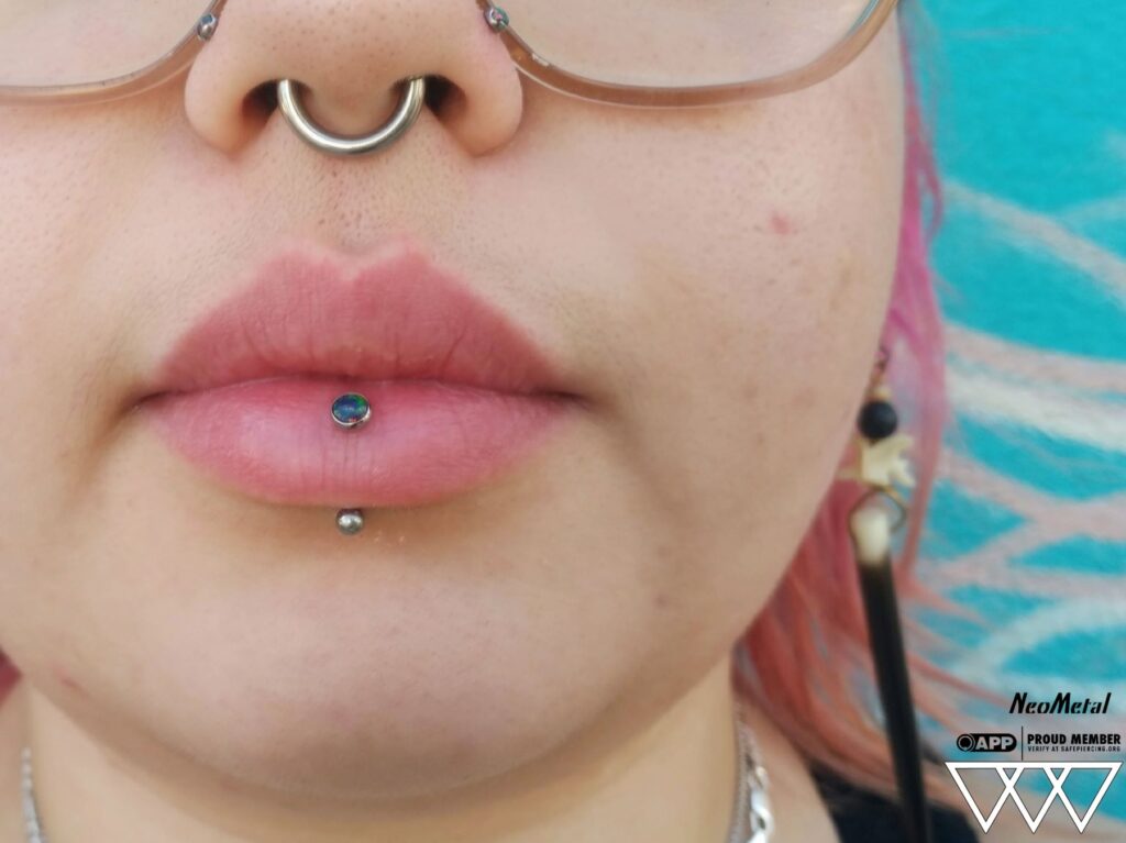Close-up of a vertical labret piercing featuring a bezel-set opal end from NeoMetal, highlighting the precise placement and the opalescent shimmer of the implant-grade titanium jewelry.