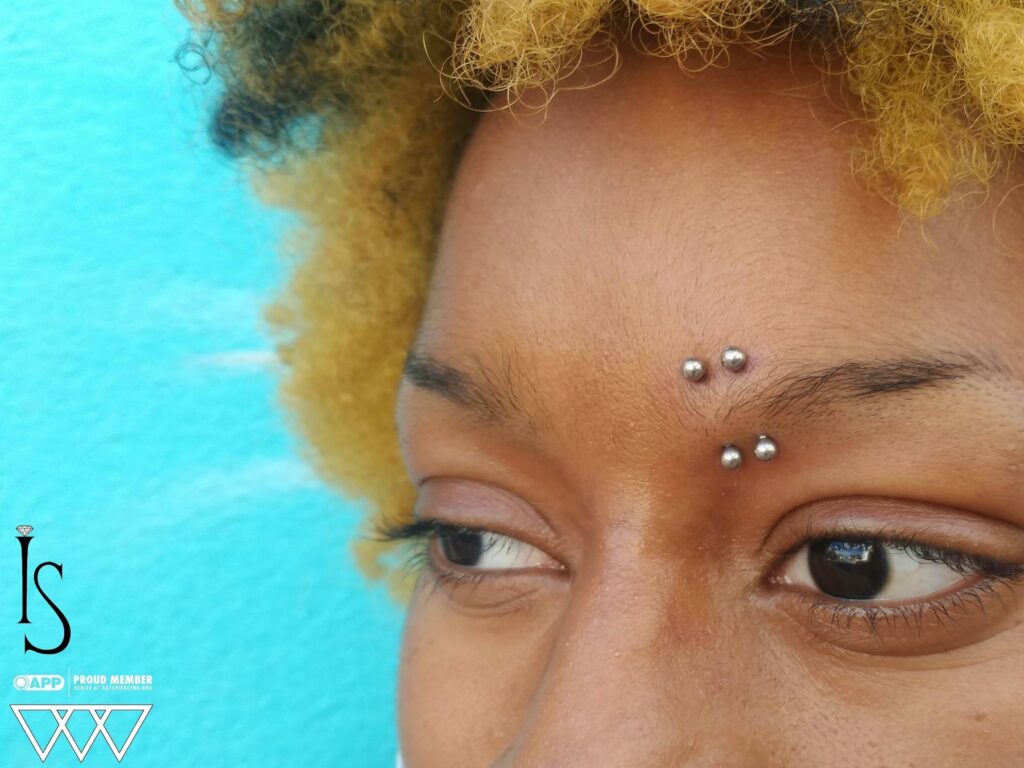 Close-up of paired inner eyebrow piercings featuring implant-grade titanium curved barbells, highlighting the symmetrical placement and polished finish.