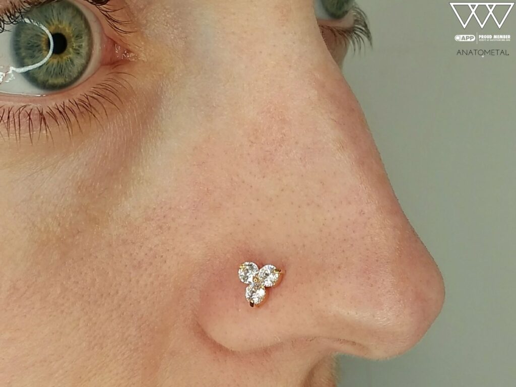 Private Body Piercing Near Manalapan – Experienced, Appointment-Only Studio Close-up of a nostril piercing adorned with an 18k rose gold 'Trio' end from Anatometal, featuring three Swarovski gemstones in a triangular arrangement, highlighting the elegant design and precise placement.