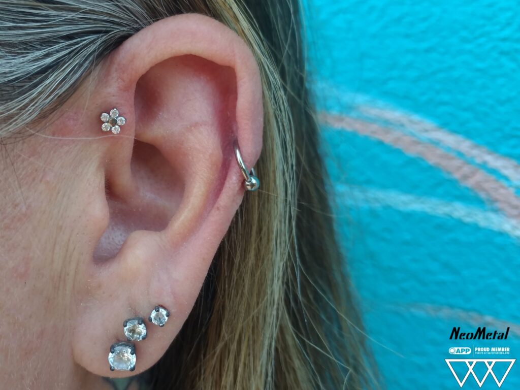 Piercing Studio for Perth Amboy. Private, Expert Care A forward helix piercing adorned with a titanium flower threadless end from NeoMetal, featuring clear Swarovski gemstones that add a delicate sparkle to the ear's upper cartilage.