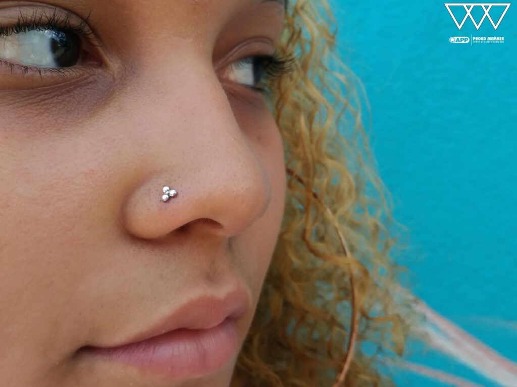 A nostril piercing upgraded with a titanium threadless 'Trinity' end from NeoMetal, featuring three bezel-set CZ Swarovski gemstones, offering a refined and symmetrical look.