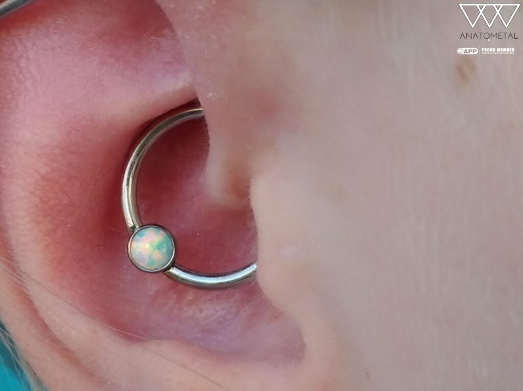 A daith piercing featuring a titanium captive bead ring with a bezel-set opal from Anatometal, offering a vibrant, budget-friendly upgrade that adds subtle sparkle to the ear's inner cartilage.