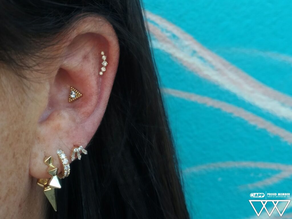 A conch piercing adorned with an 18k yellow gold 'Tryst' threadless end from Anatometal, showcasing the intricate design and precise placement on the ear's cartilage.
