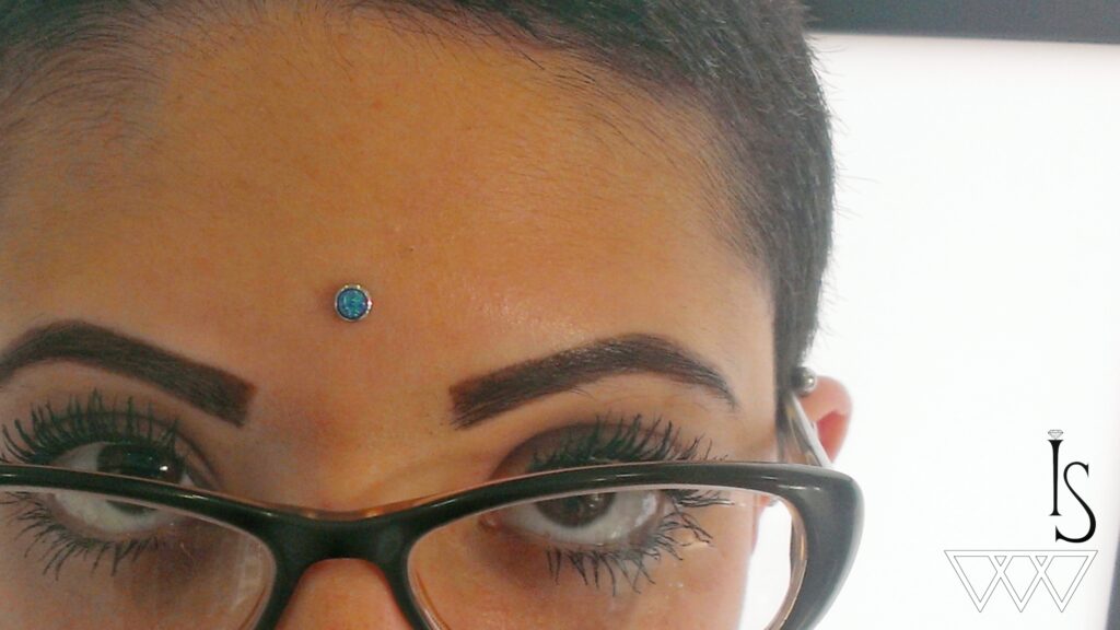 Surface Anchors in Staten Island, NYC | Professional Piercing Close-up of a forehead surface anchor featuring a teal opal end, highlighting the vibrant gemstone and centered placement above the brows.